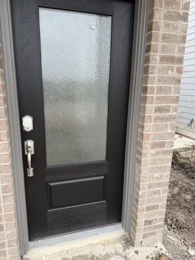 Black fiberglass entry door with textured three-quarter glass and smart lock, installed in a brick opening in San Antonio