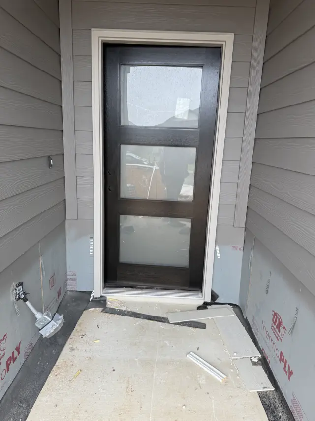Dark entry door with four frosted glass panels installed in a siding entryway